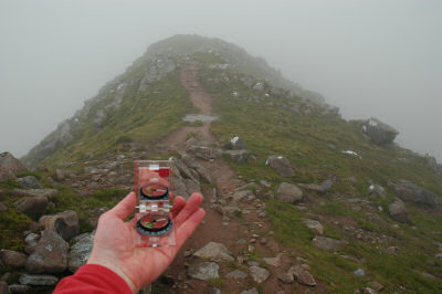 Picture of a hand holding a compass in front of a path disappearing into clouds