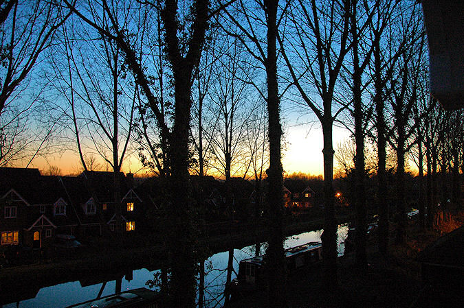 Picture of a sunset over a canal lined with trees, after the sun has set and only the gloaming remains