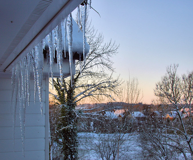 Picture of icicles hanging from a roof, a wintry landscape in the background